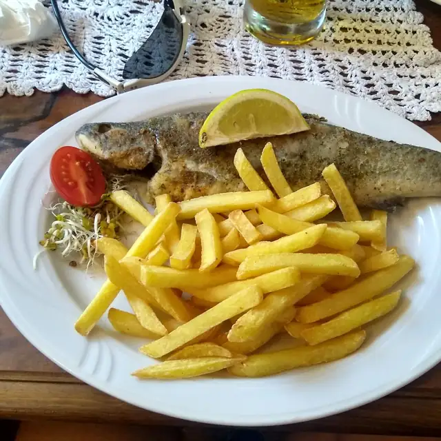 Smażona ryba z frytkami, cytryną i pomidorem na talerzu na ażurowej serwecie